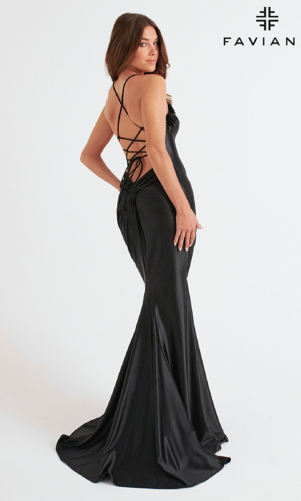 A woman in the Faviana 11249 long black satin prom dress with a lace-up open back stands against a white background. The Faviana logo is visible in the top right corner.